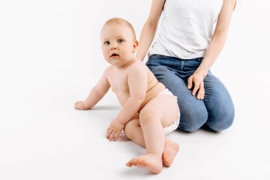 İzole edilmiş beyaz arka planda oturan, bezli, gülümseyen küçük bir bebek.