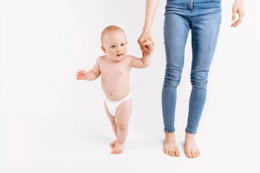 İlk adımları atan küçük çocuk, annesinin yardımıyla yürümeyi öğrenen küçük mutlu çocuk, beyaz bir arka planda, çocuğun büyüme ve gelişme kavramı,