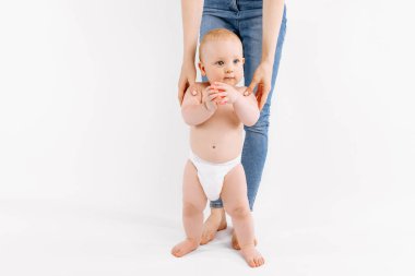 Bebek, annesinin yardımıyla izole edilmiş beyaz arka planda ilk adımı atıyor.