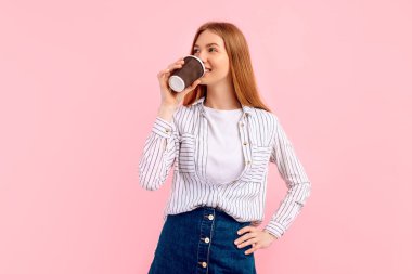 Elinde kahve fincanı tutan mutlu genç bir kadın, pembe arka planda gülümsüyor.