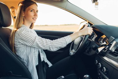 Gün batımında yeni arabasını süren güzel, mutlu, genç bir kadın.