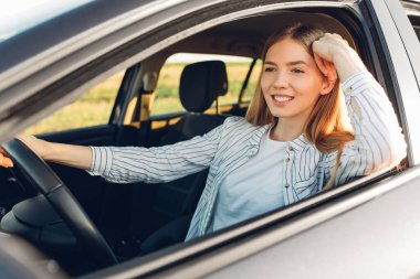 Gün batımında yeni arabasını süren güzel, mutlu, genç bir kadın.