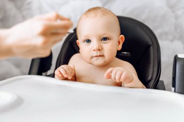 Anne kaşıktan komik bir bebeği besler, bebek sandalyede oturur.