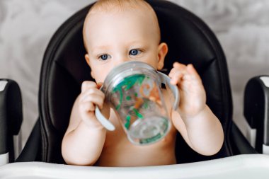 Bebek beslenme sandalyesinde oturan bebek şişesinden su içen mutlu şirin bebek.