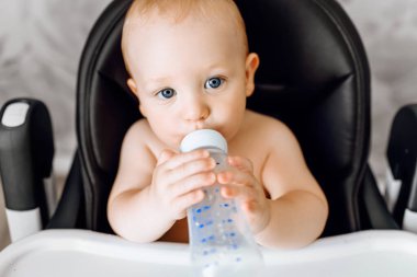 Bebek beslenme sandalyesinde oturan bebek şişesinden su içen mutlu şirin bebek.