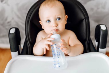 Bebek beslenme sandalyesinde oturan bebek şişesinden su içen mutlu şirin bebek.