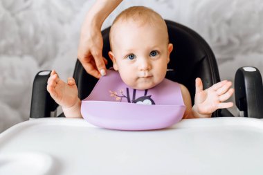 Çocuk koltuğunda yemek bekleyen gülümseyen küçük bir çocuk.