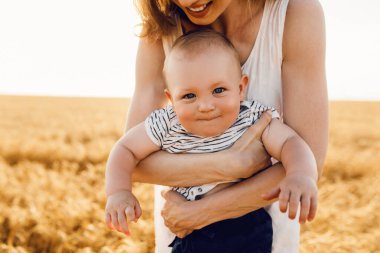 Altın buğday tarlasında bebeği, tahıl tarlasında bir ailesi olan güzel anne, küçük oğluna sarılıyor.