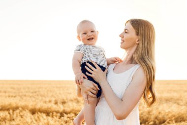 Altın buğday tarlasında bebeği, tahıl tarlasında bir ailesi olan güzel anne, küçük oğluna sarılıyor.