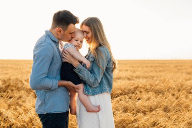 Mutlu aile, anne, baba ve küçük çocuk Olgun buğday tarlasında gün batımında