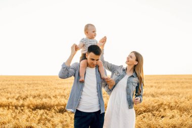 Mutlu aile, anne, baba ve küçük çocuk Olgun buğday tarlasında gün batımında