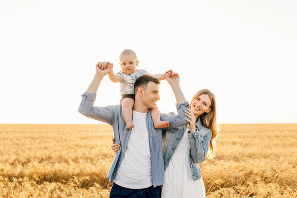 Happy family, mother, father and little child on the ripe wheat field at sunset