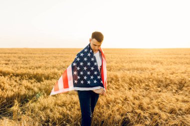 Gün batımında buğday tarlasında gururla Amerikan bayrağını sallayan genç adam.