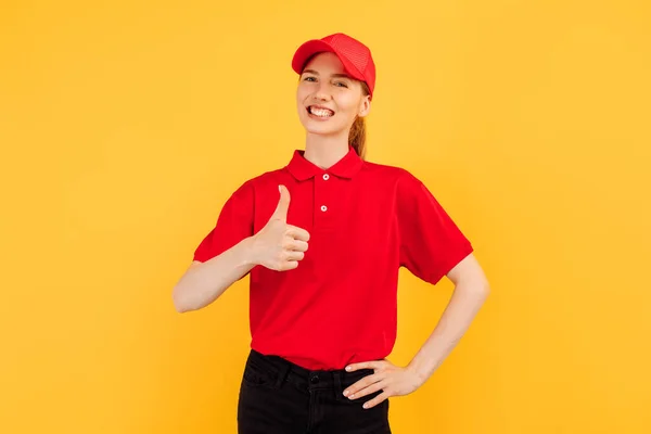 Veselá Mladá Kurýrka Červené Uniformě Ukazující Palec Nahoru Stojící Žlutém — Stock fotografie