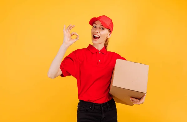 持纸盒包裹的红色制服送货 女雇员担任信使 背景为黄色 服务概念 — 图库照片