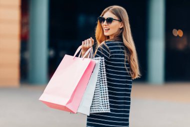 Geriye bakış, güneş gözlüklü mutlu, çekici genç bir kadın, alışveriş merkezinde alışveriş torbaları. moda