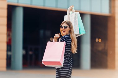 Geriye bakış, güneş gözlüklü mutlu, çekici genç bir kadın, alışveriş merkezinde alışveriş torbaları. moda