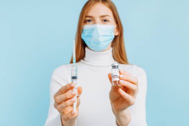 Coronavirus COVID-19 'a karşı bir aşı geliştirilmesi ve üretilmesi, tıbbi maskeli genç bir kadın, cam bir şişede Coronavirus' a karşı aşı taşıyor ve elinde mavi arka planda Coronavirus 'a karşı aşı kavramı bulunuyor.