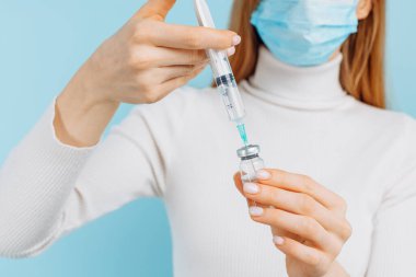 Doktor elinde bir şişe covid-19 koronavirüs aşısı ve şırınga ile bir hastaya aşı enjekte etmeye hazır, mavi arka planda, aşı konsepti.