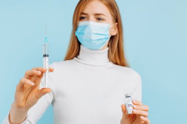 Doktor elinde bir şişe covid-19 koronavirüs aşısı ve şırınga ile bir hastaya aşı enjekte etmeye hazır, mavi arka planda, aşı konsepti.