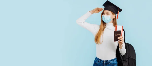 Happy young woman student in medical mask, student in graduation hat holding passport and tickets on blue background, Study, education, university, admission