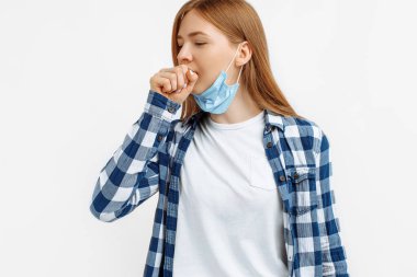 Tıbbi koruyucu maskeli genç bir kadın öksürükten muzdarip ve beyaz arka planda kendini kötü hissediyor.