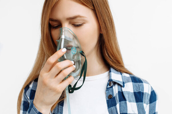 Молодая женщина держит маску для вдыхания перед лицом, на белом фоне лечение болезни легких