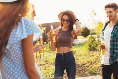 Bir grup mutlu genç arkadaş yaz güneşli bir günde doğada dinleniyor, içki, tost, kutlama konseptini kutluyorlar.