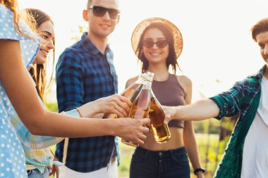 Bir grup mutlu genç arkadaş yaz güneşli bir günde doğada dinleniyor, içki, tost, kutlama konseptini kutluyorlar.