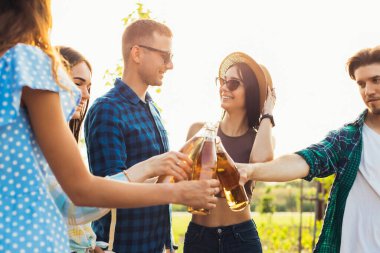 Bir grup neşeli genç arkadaş parti veriyor, birlikte soğuk içecekler içiyorlar, güneşli bir yaz gününü dışarıda kutluyorlar.