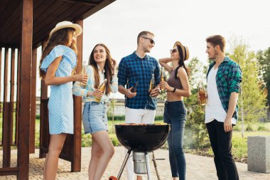 Genç arkadaşlar barbekü yaparken et pişirirken eğleniyorlar, bir grup mutlu kız ve erkek dışarıda barbekü yemeği hazırlayıp yiyorlar, erkekler ve kadınlar ızgaranın etrafında durup sohbet ediyorlar..