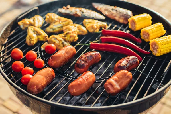 夏には公園の屋外で煙と炎で焼き野菜とおいしい品揃えのグリル肉やソーセージ — ストック写真