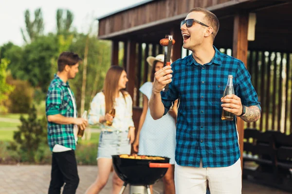 Young happy man in sunglasses having a group of friends having a barbecue with beer drinks having a rest in nature on a sunny day