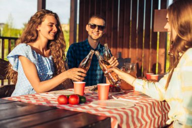 Genç arkadaşlar eğleniyor, açık havada içki içiyor, mutlu insanlar doğada, gün batımında birlikte barbekü yiyorlar.