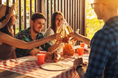 Bir grup arkadaş, genç erkekler ve kadınlar doğada barbekü yapıyorlar, mutlu insanlar masada oturup yemek yiyorlar, piknikte eğleniyorlar, yaz zamanı konsepti, arkadaşlık