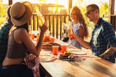 Mutlu bir arkadaş grubu arka bahçe partisinde eğleniyor gençler birlikte gülüyor, bira içiyor ve dışarıda yemek yiyor.