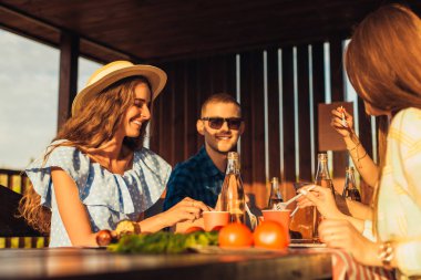 Genç arkadaşlar eğleniyor, açık havada içki içiyor, mutlu insanlar doğada, gün batımında birlikte barbekü yiyorlar.