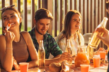 Bir grup arkadaş, genç erkekler ve kadınlar doğada barbekü yapıyorlar, mutlu insanlar masada oturup yemek yiyorlar, piknikte eğleniyorlar, yaz zamanı konsepti, arkadaşlık