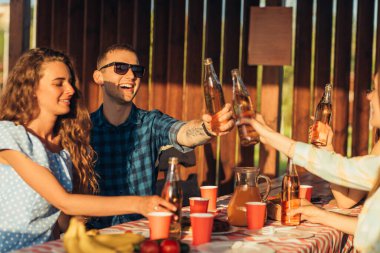 Genç arkadaşlar gün batımında kutlama yapar, içkilerle kadeh kaldırır, terasta mutlu insanlar barbekü yer, arkadaşlık kavramı yaratır.