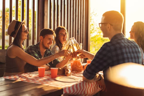 Bir grup arkadaş, genç erkekler ve kadınlar doğada barbekü yapıyorlar, mutlu insanlar masada oturup yemek yiyorlar, piknikte eğleniyorlar, yaz zamanı konsepti, arkadaşlık