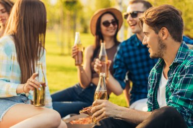 Bir grup arkadaş güneşli bir günde parkta piknik yapıyor, insanlar dışarıda takılıyor, ızgara yapıp rahatlarken eğleniyor, pizza yiyor ve içki içiyor. Güneşli bir yaz gününde