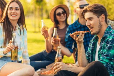 Bir grup arkadaş güneşli bir günde parkta piknik yapıyor, insanlar dışarıda takılıyor, ızgara yapıp rahatlarken eğleniyor, pizza yiyor ve içki içiyor. Güneşli bir yaz gününde