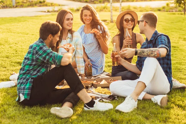芝生の上の公園でピクニックをしている若い学生を笑顔にし 若い友人は暖かい晴れた日にピザを食べて屋外で飲み物を飲む — ストック写真