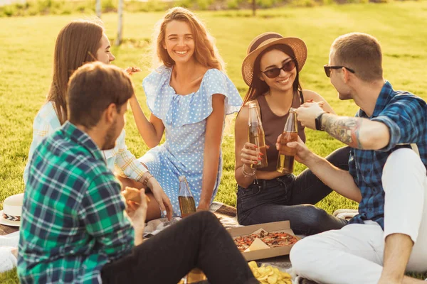 Smiling young students having a picnic in the park on the grass, Young friends enjoying warm sunny days eating pizza and drinking drinks outdoors