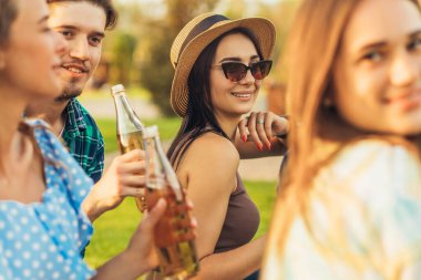 Bir yaz parkında piknik yapan bir grup arkadaş, kadeh kaldırırken bira içen arkadaşlar, çimlerin üzerinde otururken eğlenen ve kutlayan arkadaşlar, arkadaşlık, eğlence ve yemek kavramı.