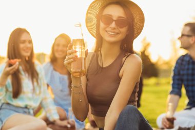 Yazlık şapkalı ve gözlüklü güzel bir kadın arkadaşlarıyla dinleniyor parkta piknikte çimlerde oturuyor yaz pikniği yapıyor.