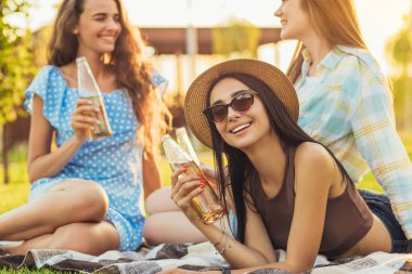 Güneşli bir yaz gününde parkta çimlerin üzerinde otururken piknikte sohbet edip eğlenen genç ve güzel kadınların görüntüsü.
