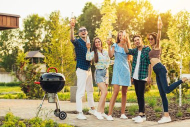 Bir grup neşeli genç arkadaş dışarıda barbekü yapıp kokteylleri kutluyor ve yaz tatilinde parkta eğleniyorlar.