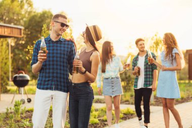 Bir yaz parkında birlikte yürüyen mutlu genç öğrenciler. Gün batımında dışarıda yürüyen ve içki içen bir grup genç insan.