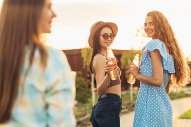 Üç güzel gülümseyen genç bayan arkadaş parkta yürüyor, bira içiyor, zafer ve arkadaşlık kavramı